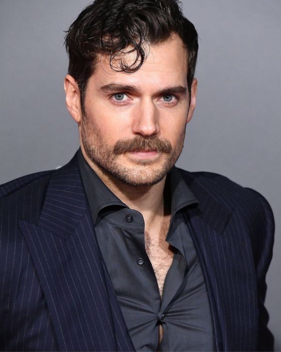 Man with a thick chevron mustache and short stubble beard wearing a pinstripe suit.