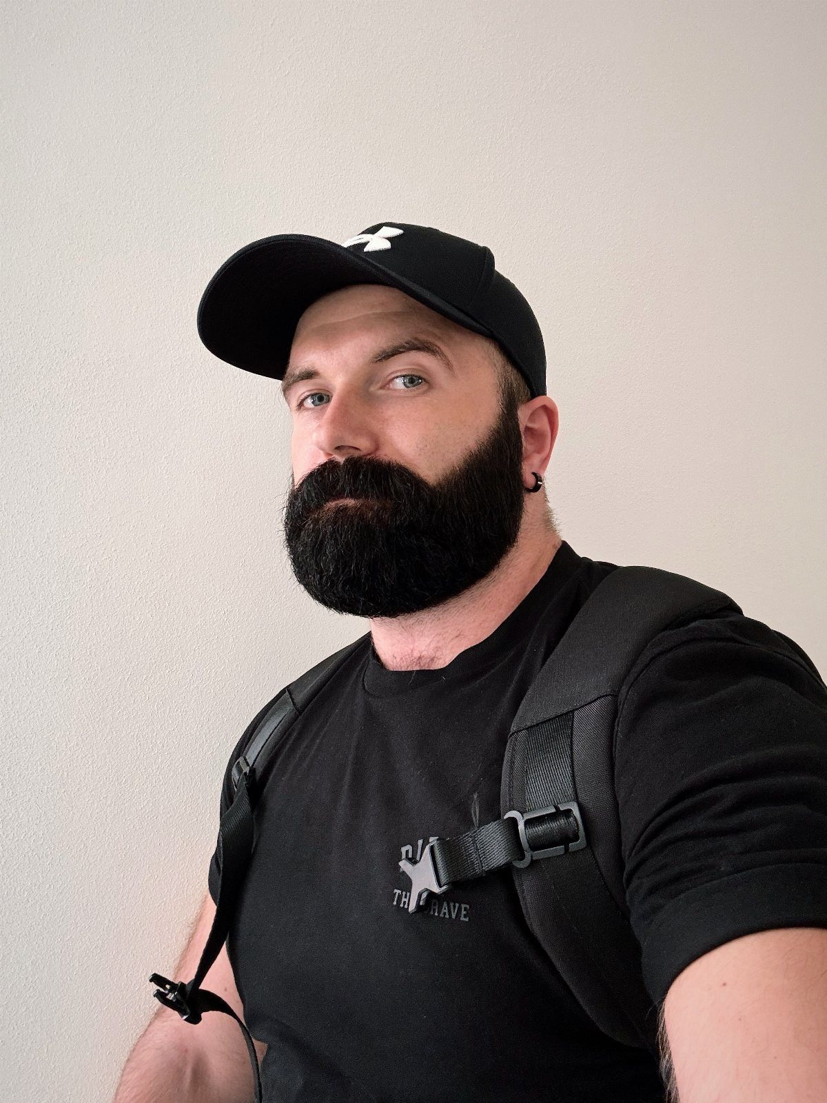 Man with a full black beard and mustache wearing a black cap and t-shirt.