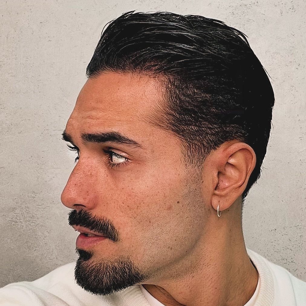 Man with slicked back hair and a groomed goatee and mustache in profile.