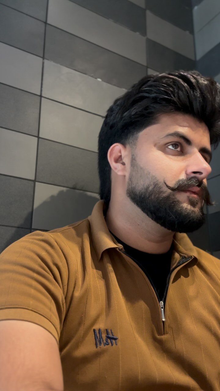 Man with a full dark beard and long curled handlebar mustache wearing brown shirt.