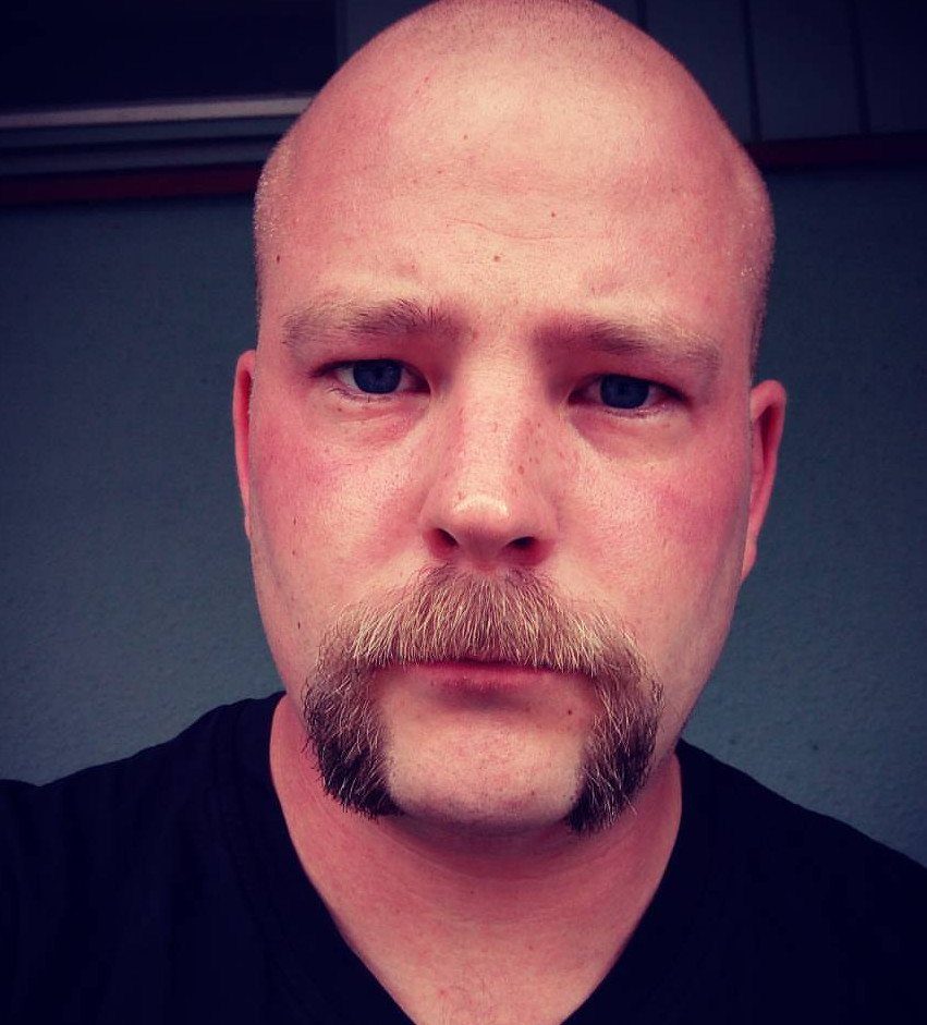 Bald man with a light-brown horseshoe mustache curving down the sides of his mouth.