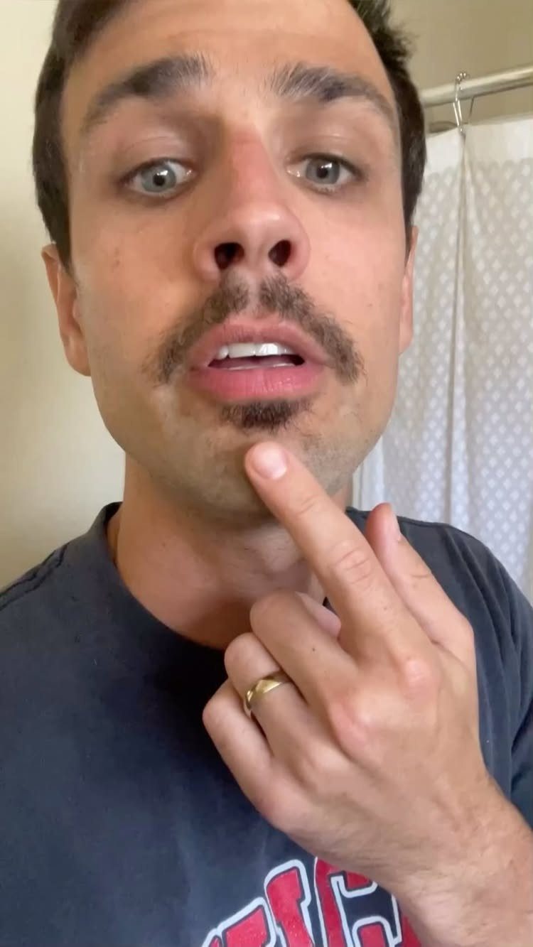 Man with a brown mustache and soul patch pointing to his chin.