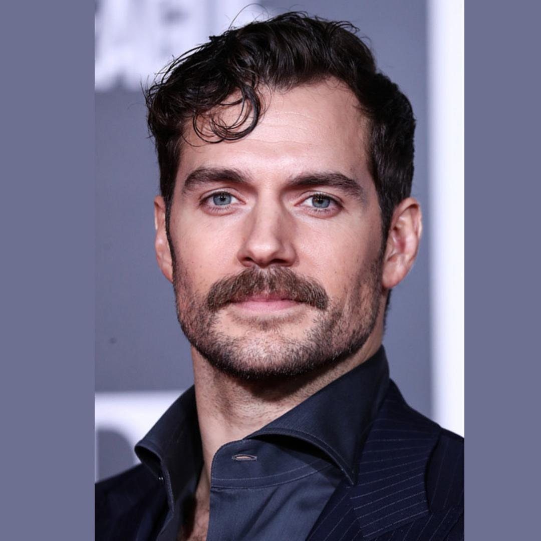 Man with a thick brown mustache and short stubble wearing a navy pinstripe suit.