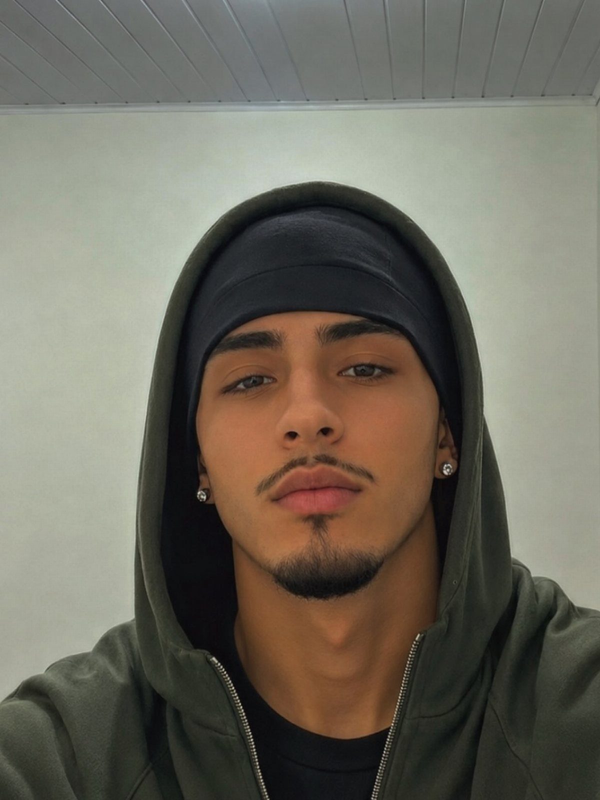 Young man with a groomed goatee and mustache wearing an olive green hoodie.