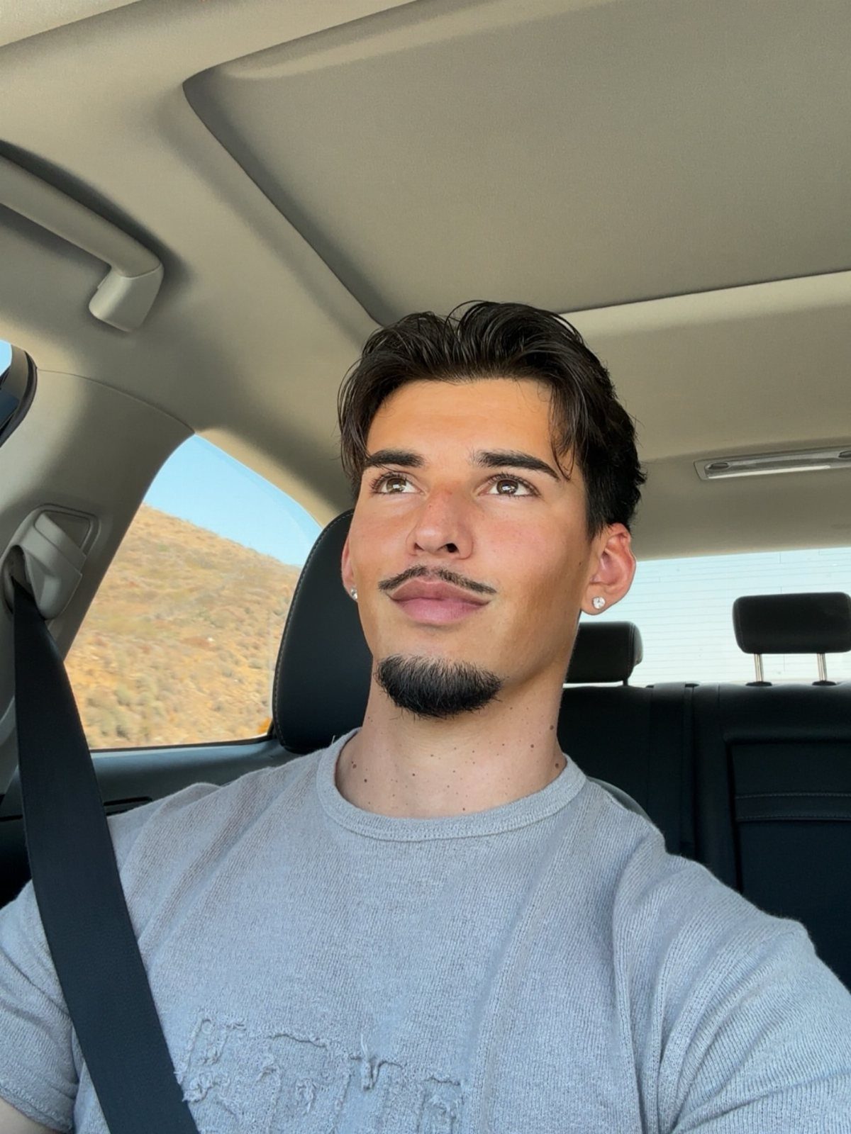Man with a petit goatee and mustache sitting inside a car.