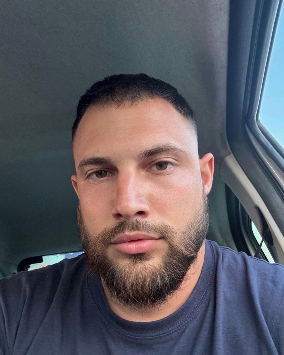 Man with a groomed boxed beard and short hair inside a car.
