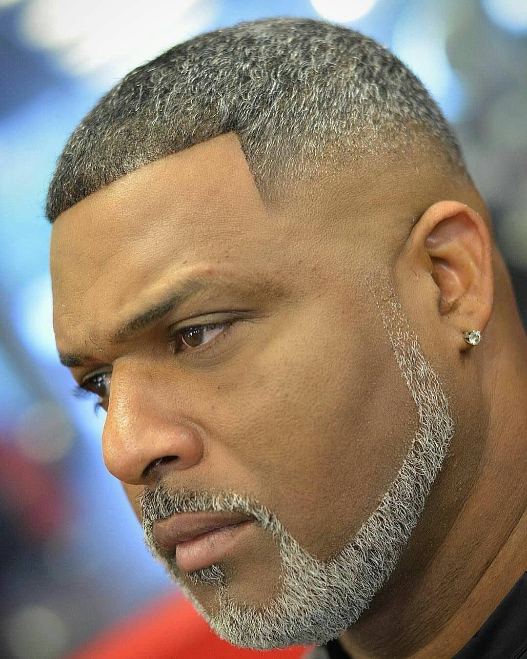 Man with a grey chin strap beard and faded haircut looking sideways.