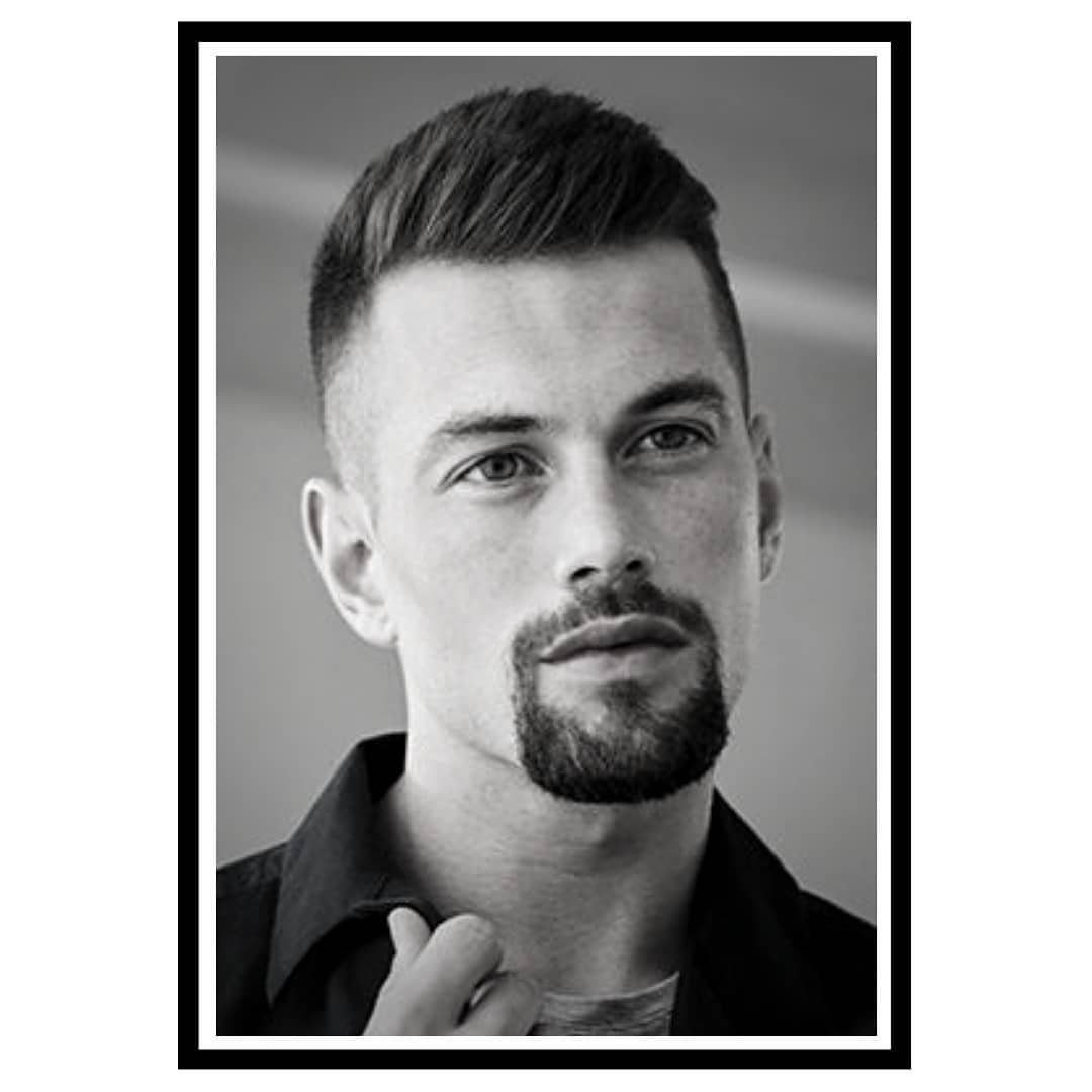 Man with a groomed circle beard and short hair in a black and white portrait.