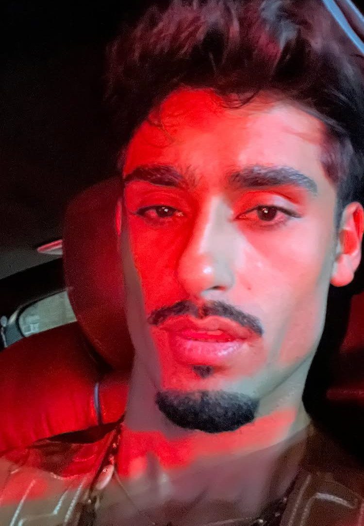Man with a dark goatee and mustache illuminated by red light in a car