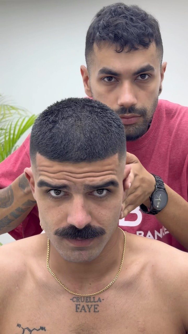 Man with a buzz cut fade and mustache posing with his barber.