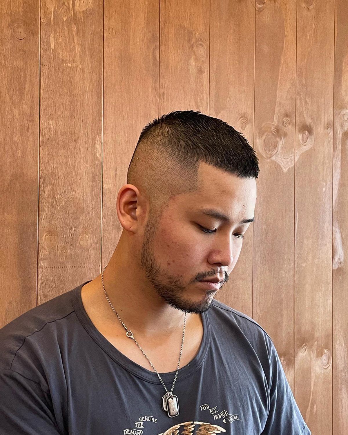 Man with a crew cut hairstyle and faded sides against a wooden wall.