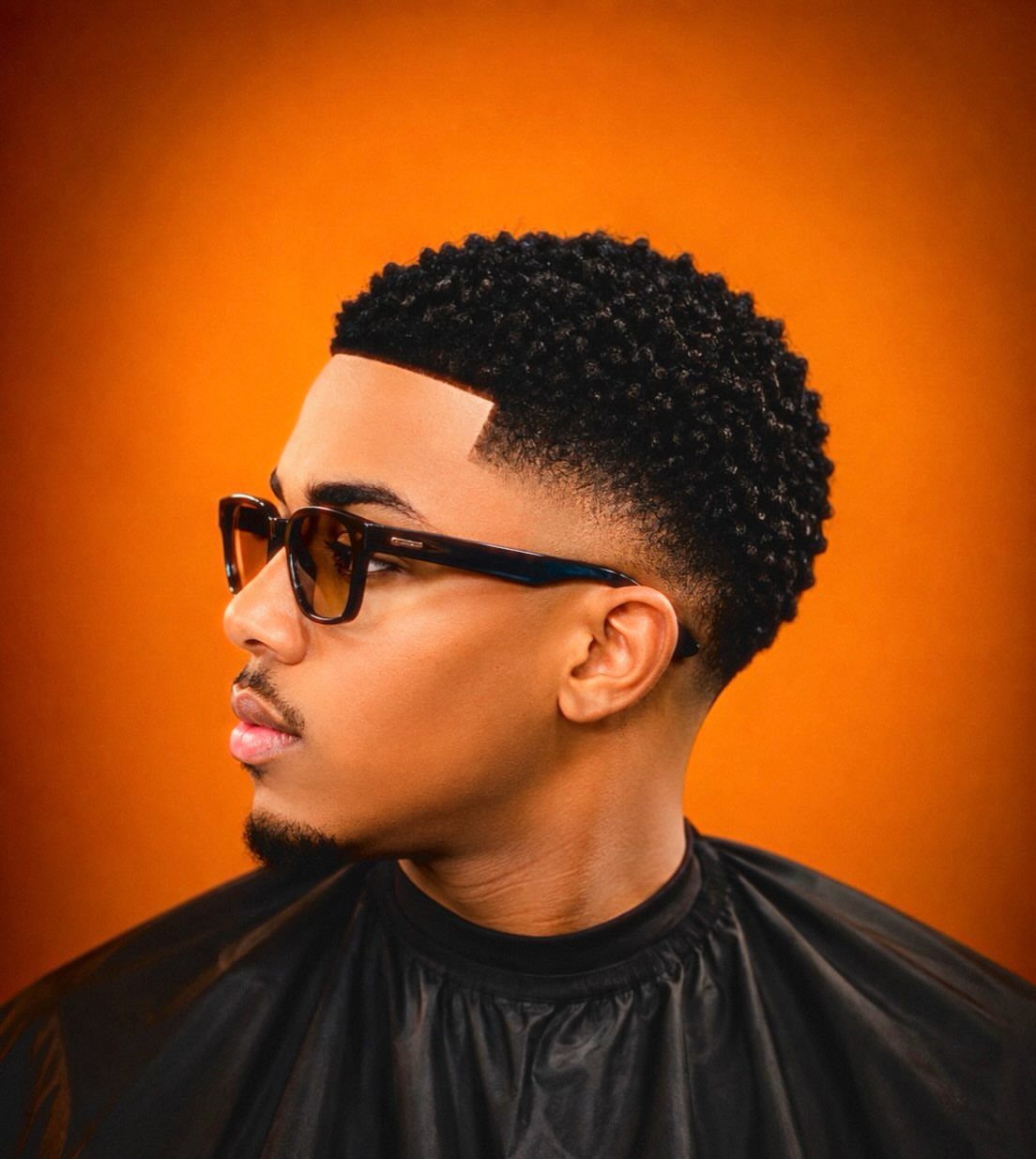 Man with curly hair and a short fade haircut wearing black glasses.