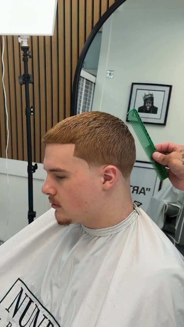 Young man with a low fade buzz cut wearing a white barber cape.