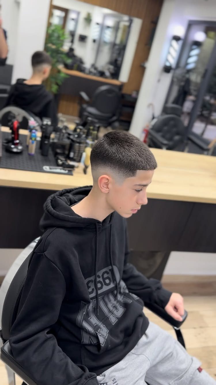 Young man with a buzz cut and mid fade sitting in a barbershop.