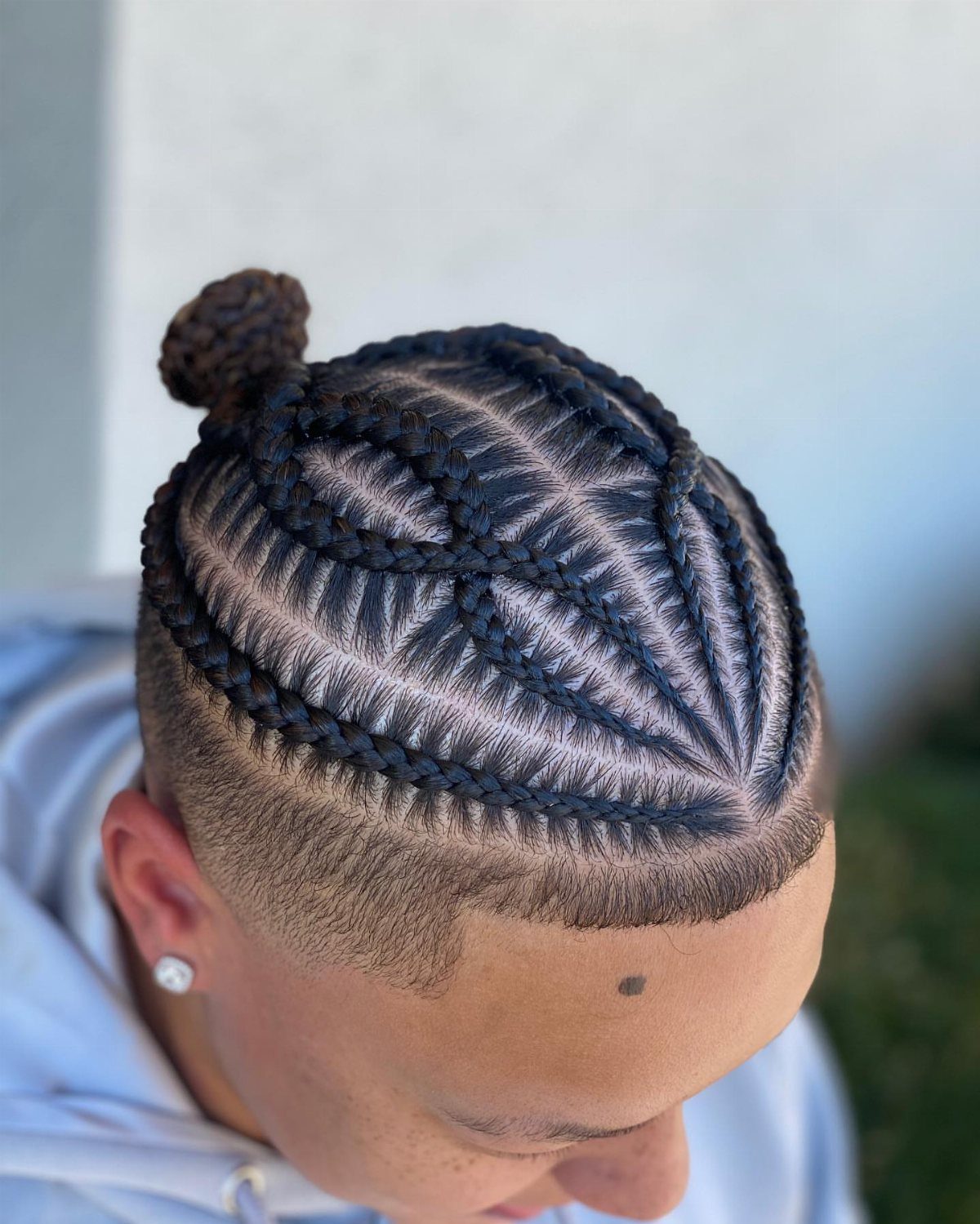 Man with intricate curved cornrow braids gathered into a small bun on top.