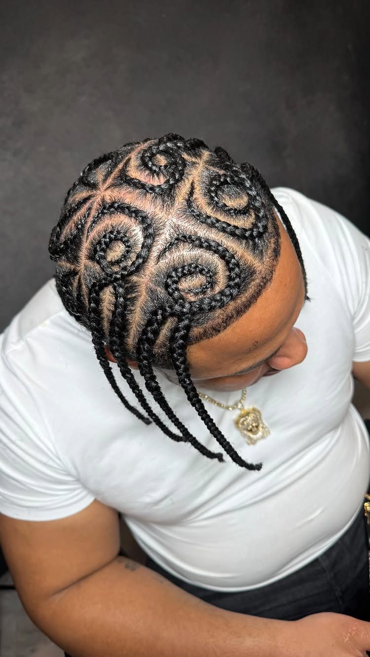Man with black hair styled in swirling cornrow braids wearing a white t-shirt.