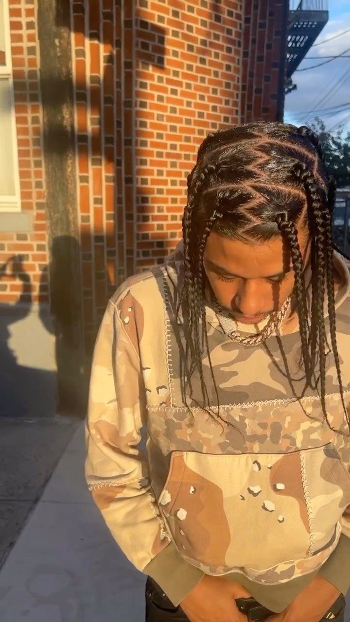 Man with cornrows transitioning into box braids wearing a camouflage hoodie outdoors.