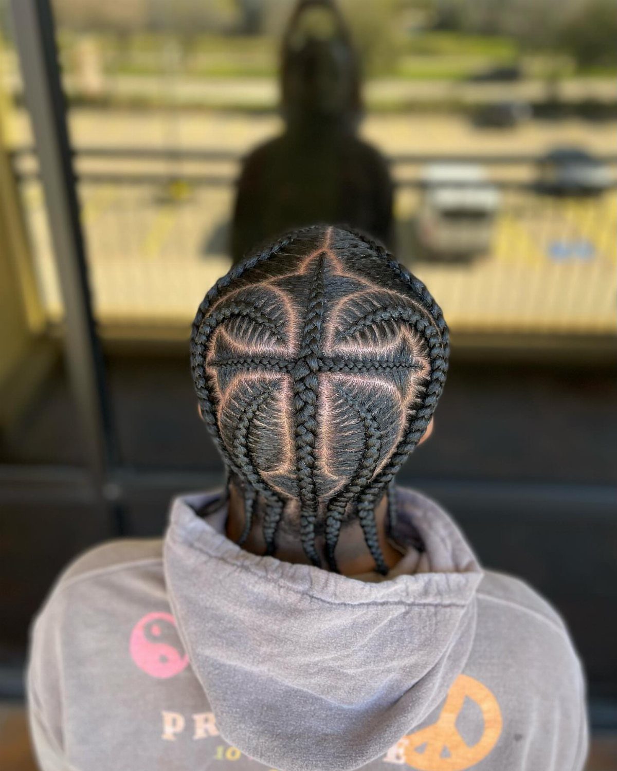 Back view of a person with cornrows braided in a crossed star pattern.