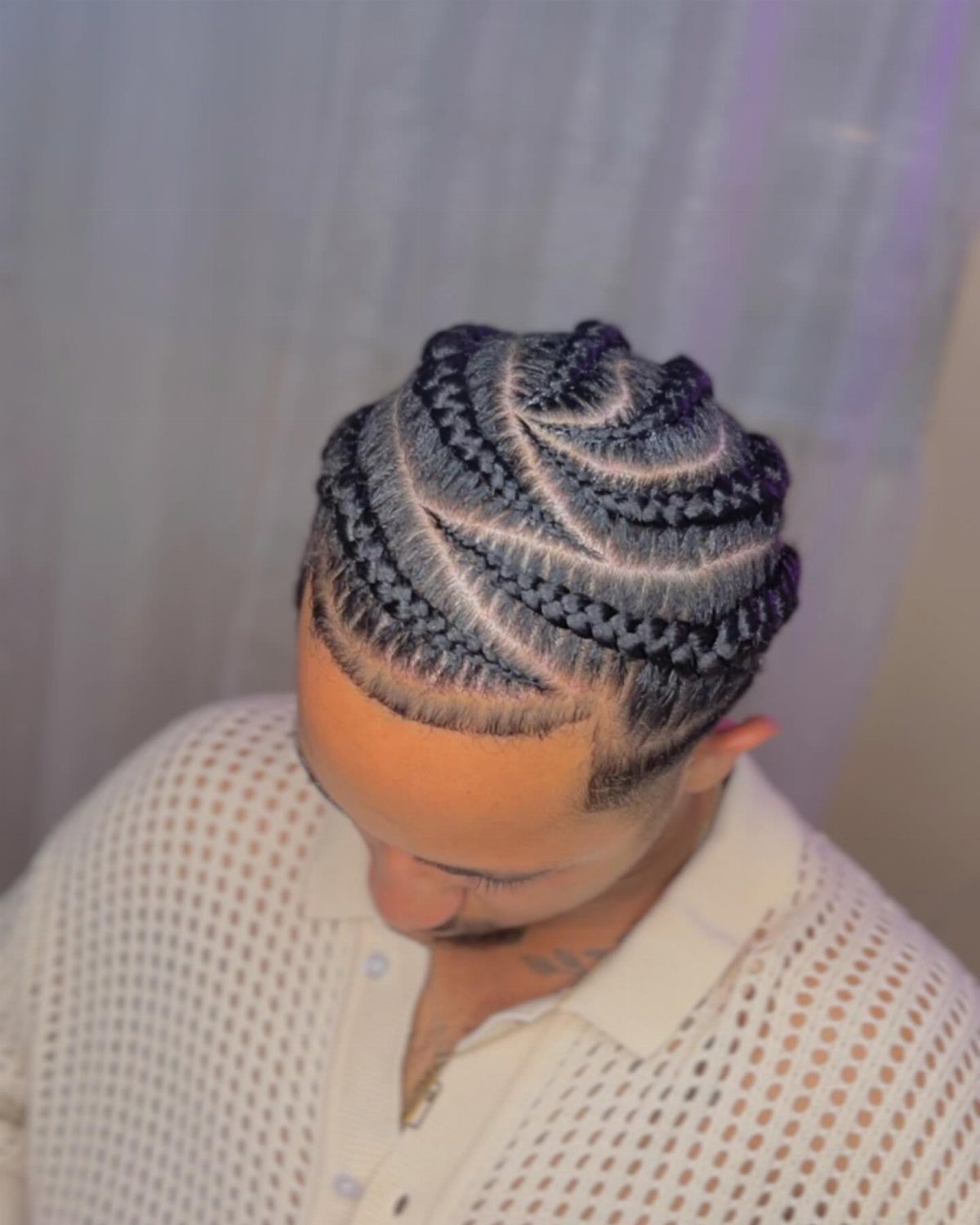 Man with curved cornrow braids on top and short faded sides.