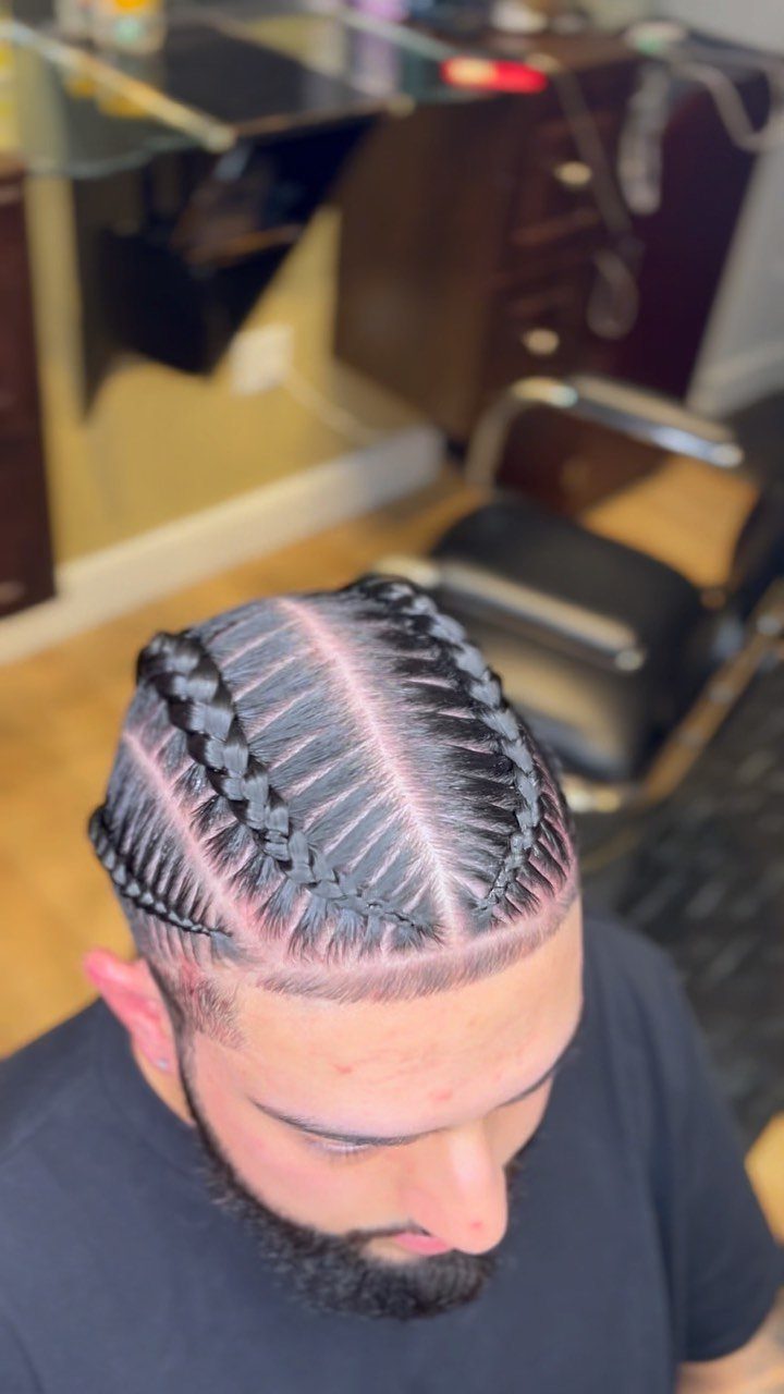 Man with stitch cornrows and a groomed beard in a barbershop setting.