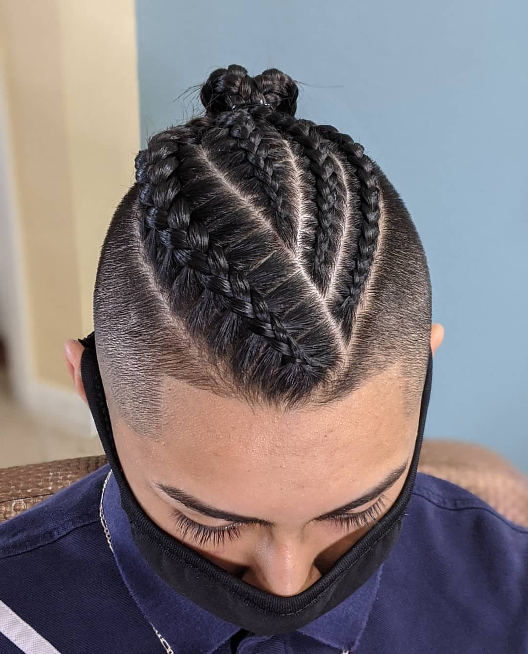 Man with cornrows tied into a top knot bun and a faded undercut.