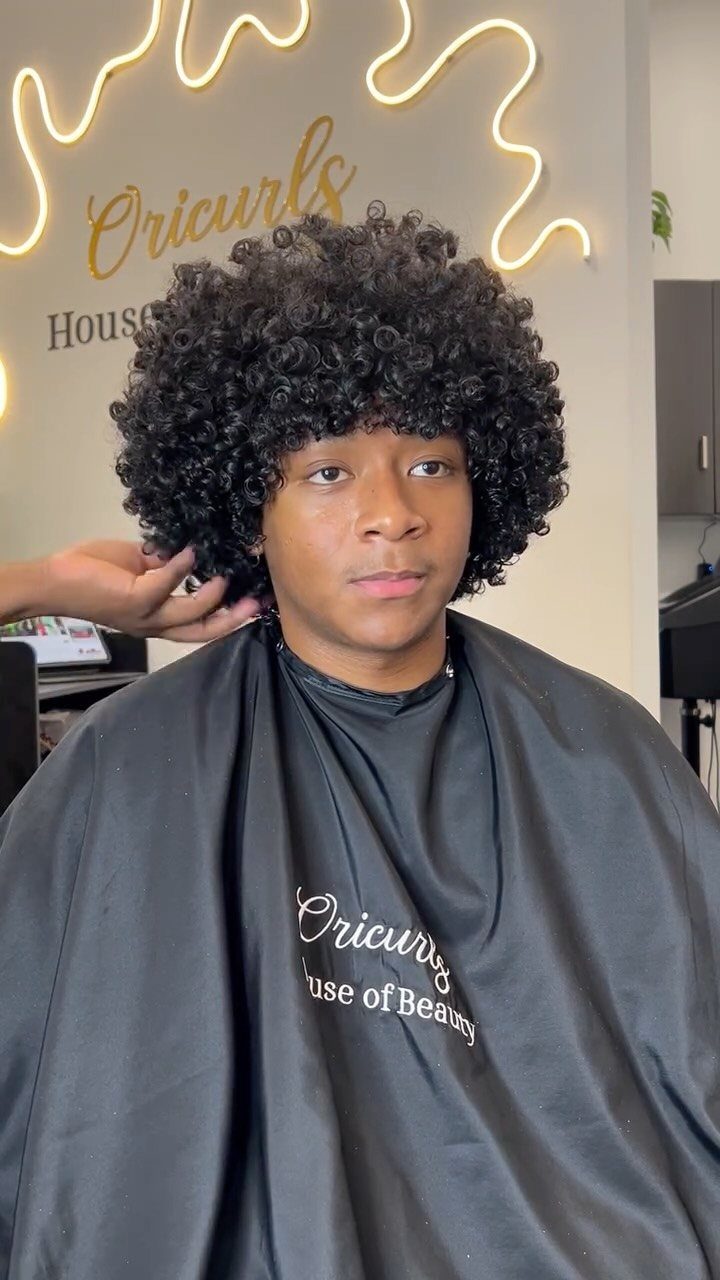 Young man with a large, rounded black curly afro in a beauty salon.