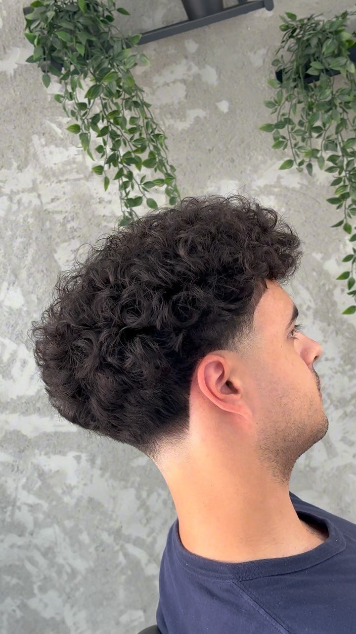 Man with a curly burst fade haircut and voluminous dark curls on top.