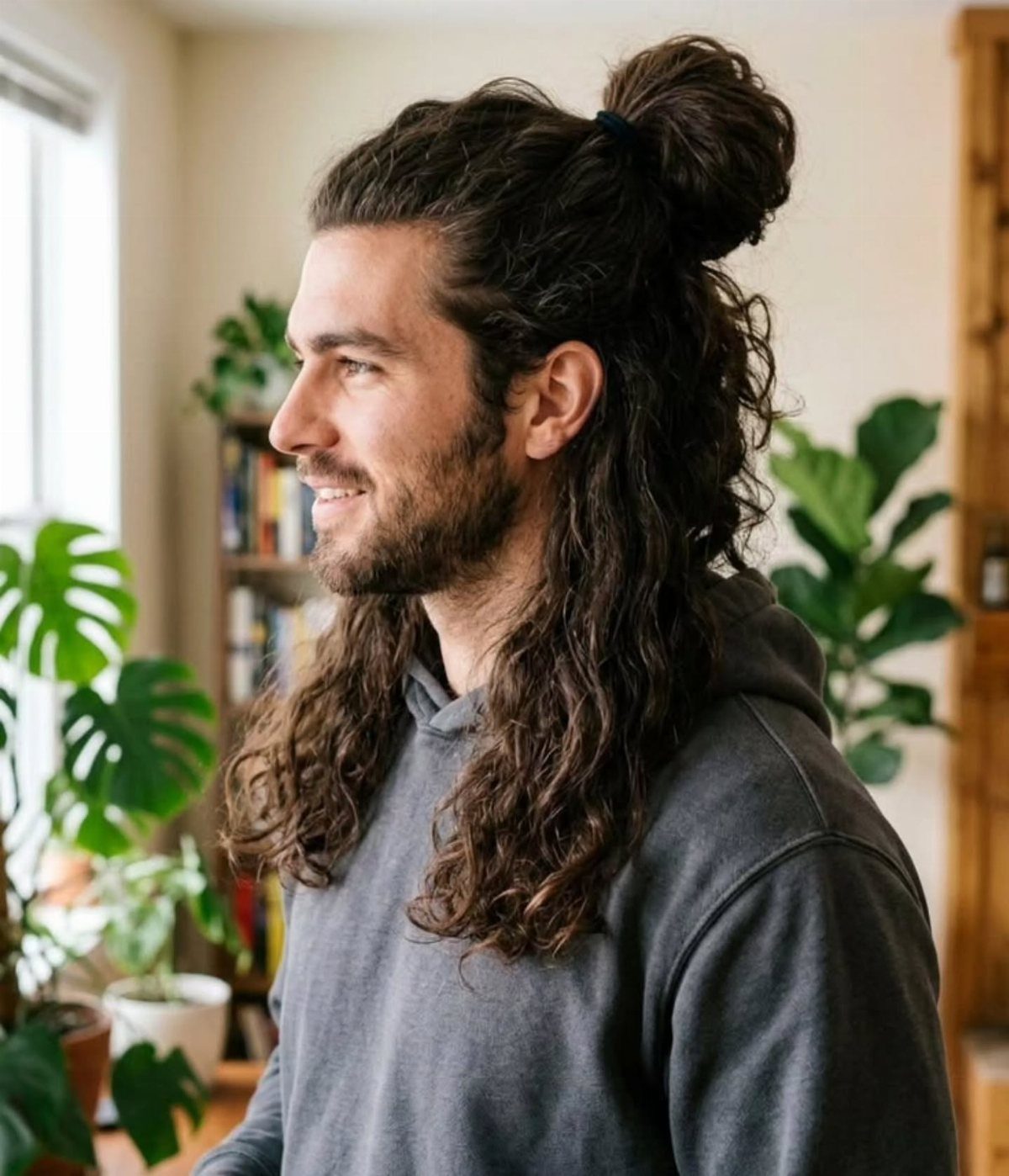 Man with long dark curly hair tied into a high man bun