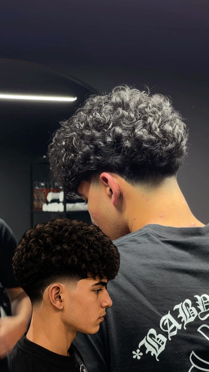 Two young men with curly hair and tapered haircuts in a barbershop setting.