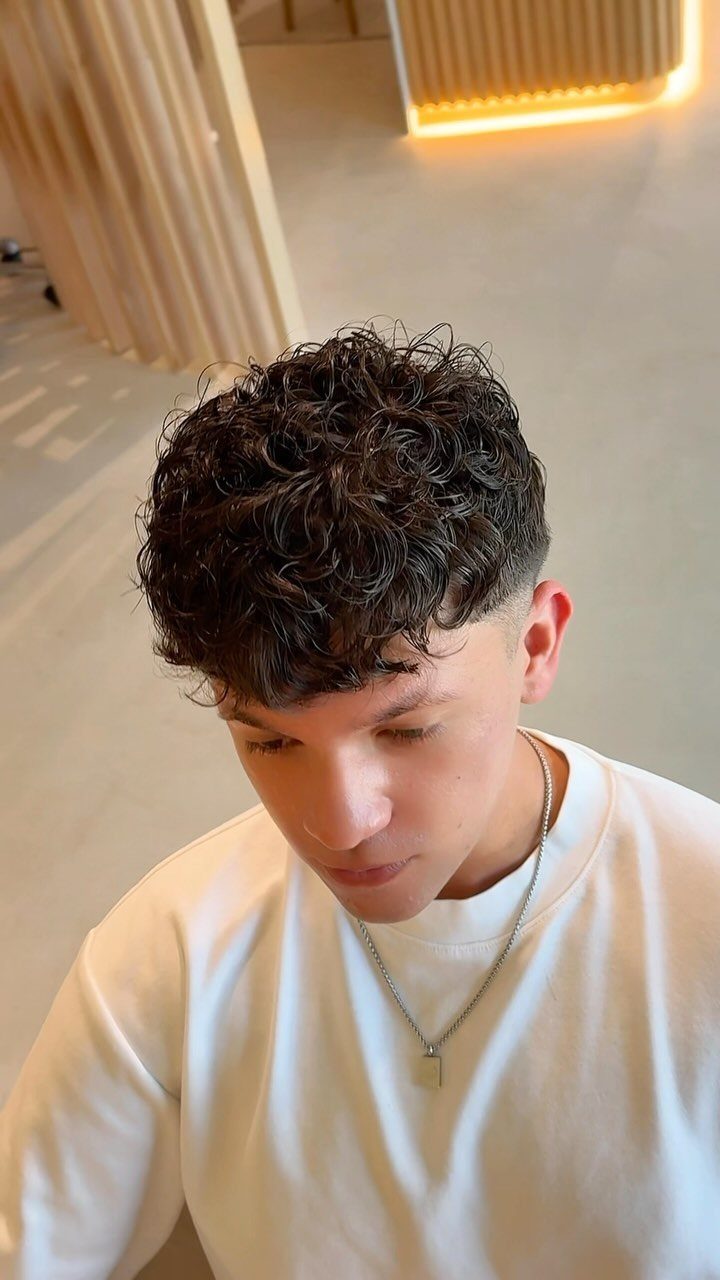 Young man with a curly undercut haircut, dark curls on top and faded sides.