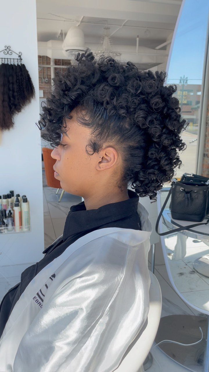 Person with tight dark curls styled into a faux hawk in a salon.