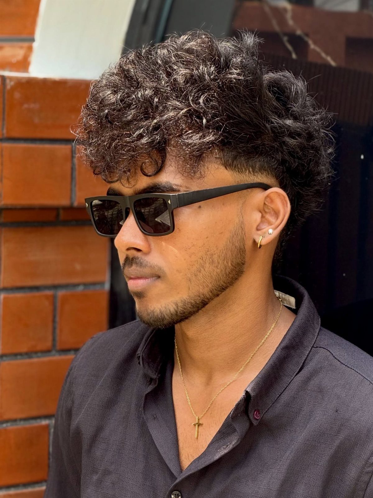 Man with a curly modern mop top haircut and tapered sides wearing sunglasses.