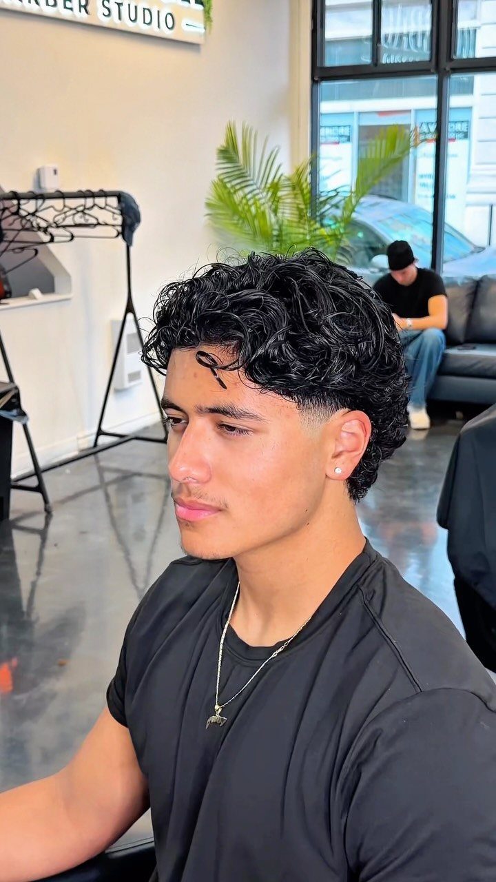 Young man with dark curly hair and tapered sides in a barber studio.
