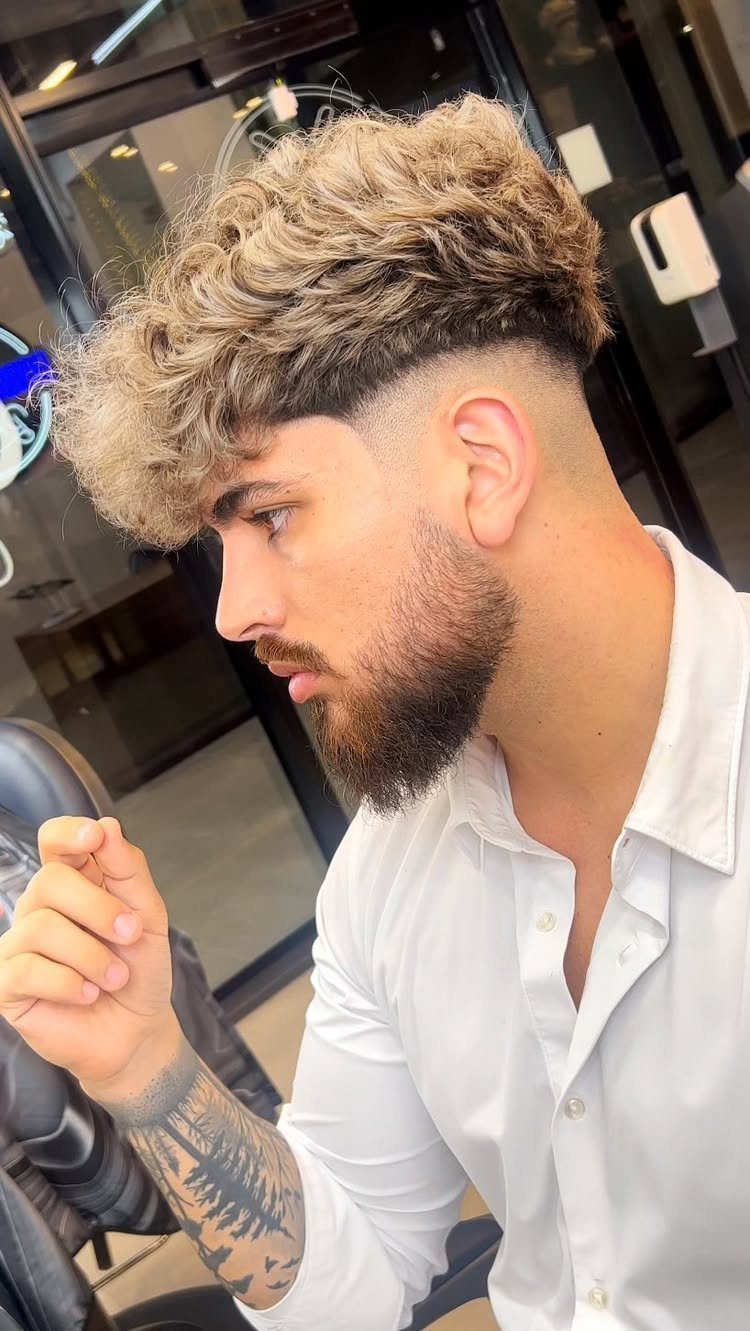 Man with textured curly blonde hair on top and buzzed faded sides.