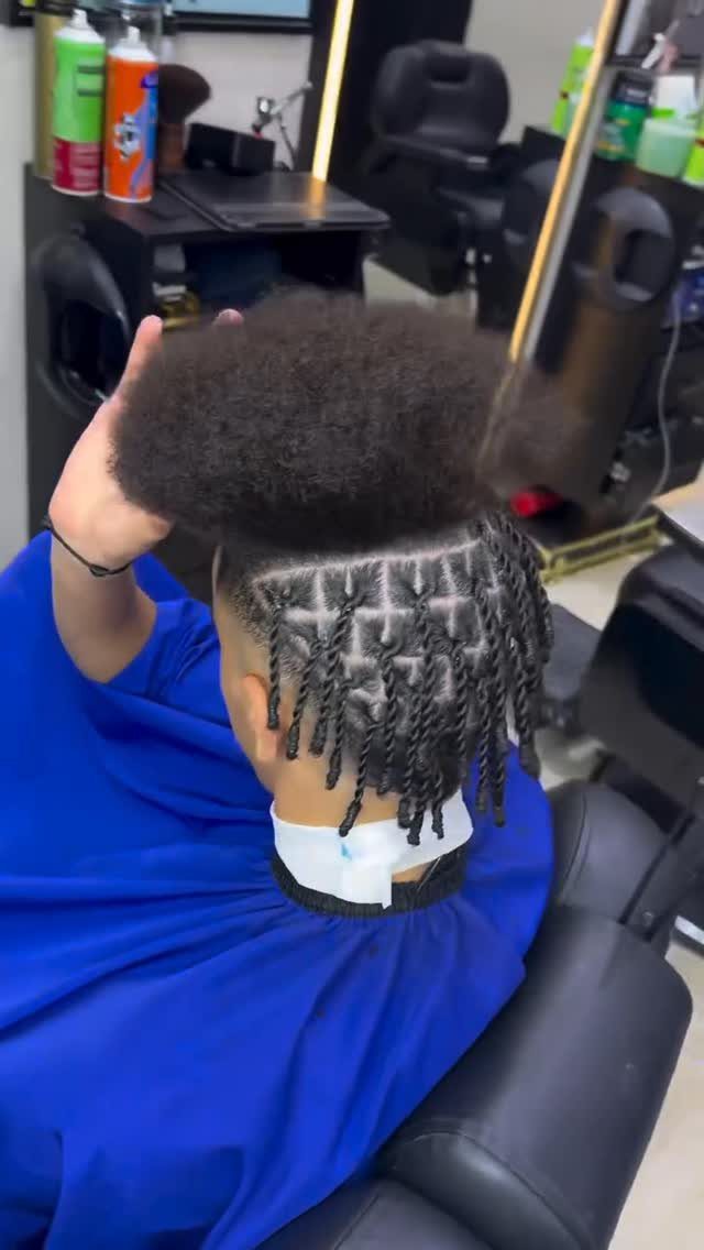 Man with a high top afro and short dreadlocks sitting in a barber chair