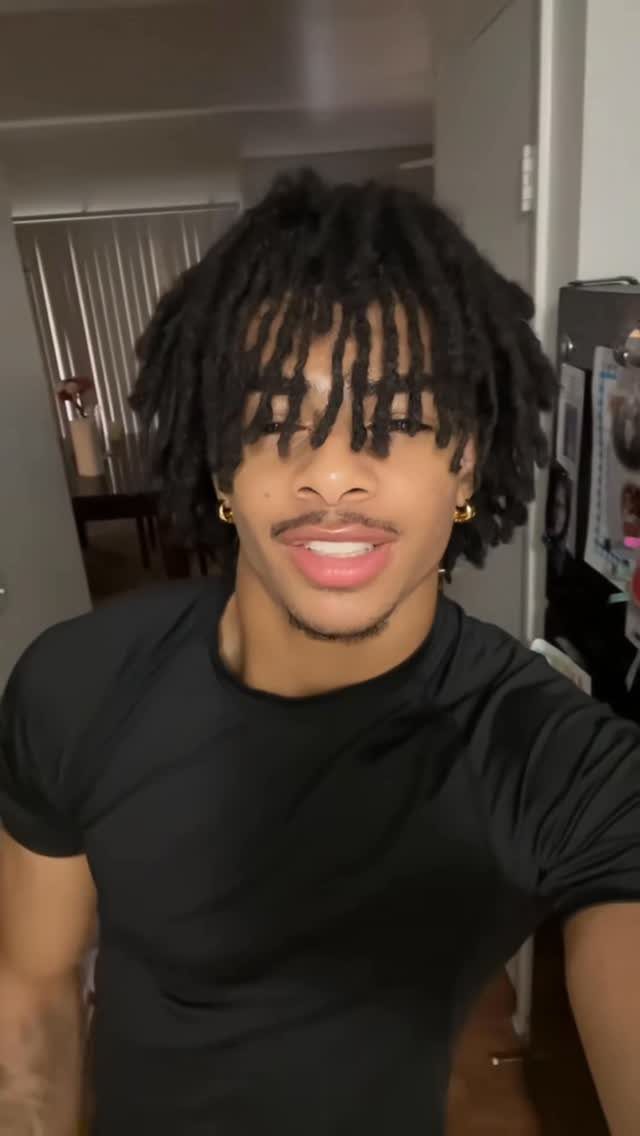 Young man with thick, chunky black dreadlocks and gold hoop earrings smiling.