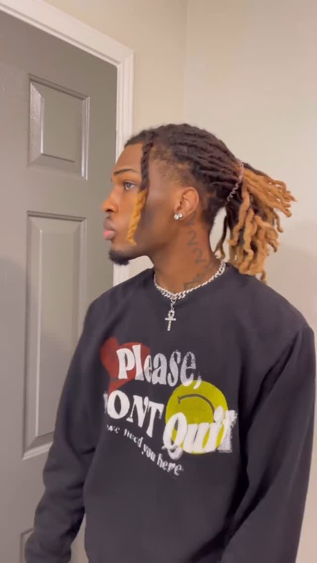 Man with blonde-tipped dreadlocks tied in a low ponytail wearing a black sweatshirt.