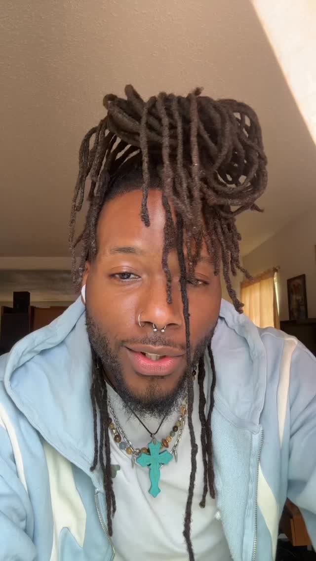 Man with brown dreadlocks styled into a high bun and loose hanging locs.