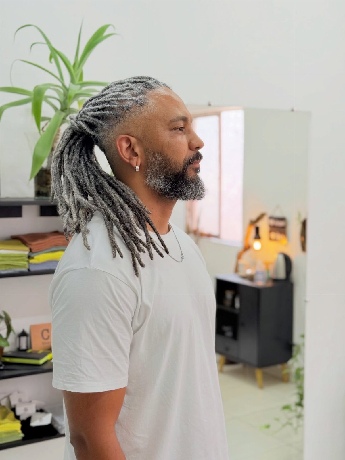 Man with long grey dreadlocks tied back and a taper fade haircut.