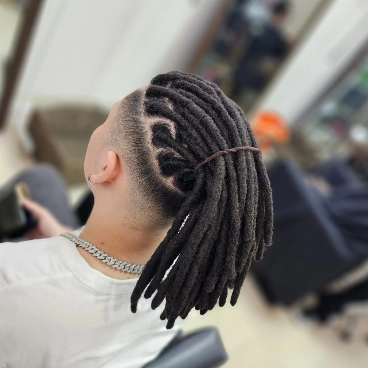 Man with dark brown dreadlocks tied back and a shaved undercut side profile.