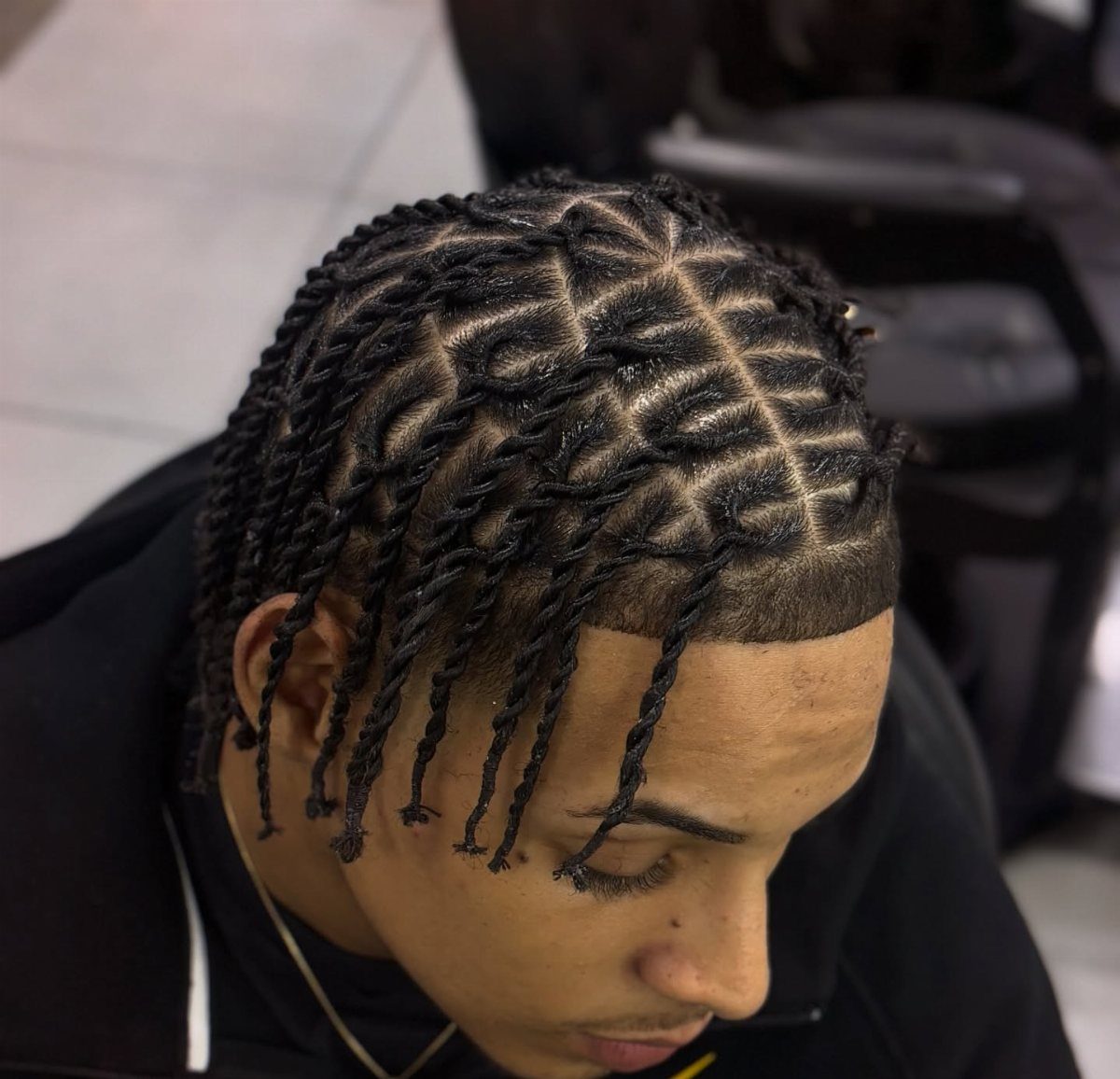 Man with black twisted dreadlocks and geometric scalp parting wearing a black hoodie.
