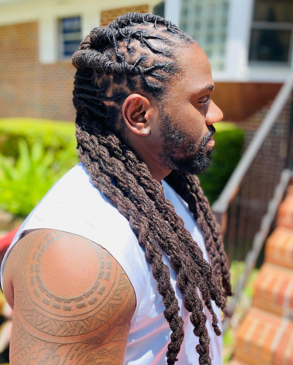 Man with long dark brown dreadlocks and a beard posing outdoors.