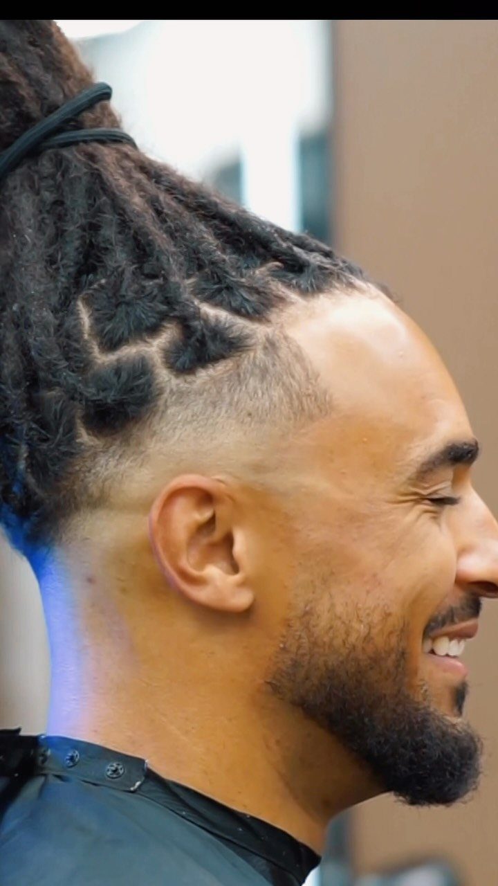 Man with dark dreadlocks tied into a high ponytail and a side fade.