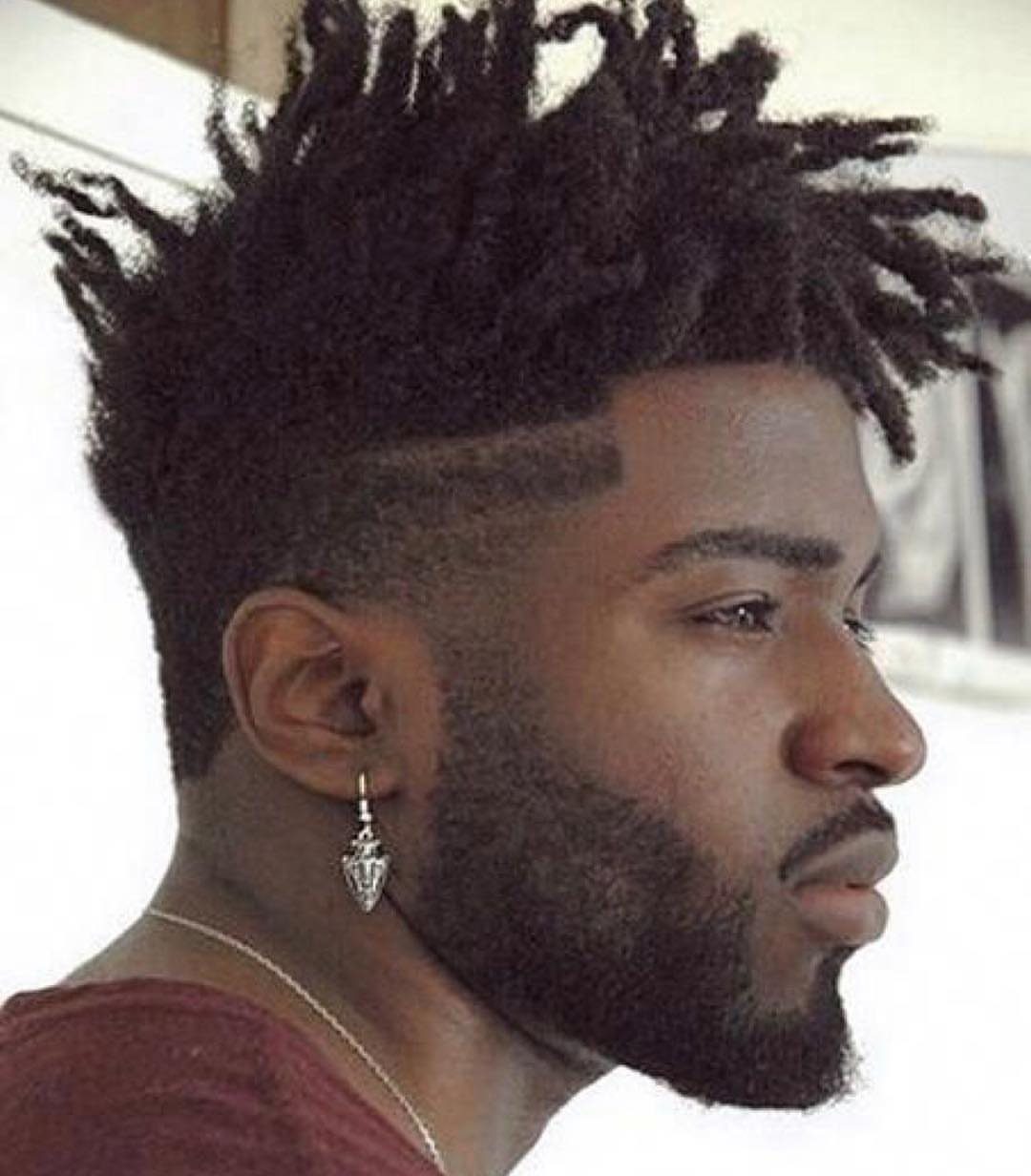 Man with short black dreadlocks styled in a high top with a fade.