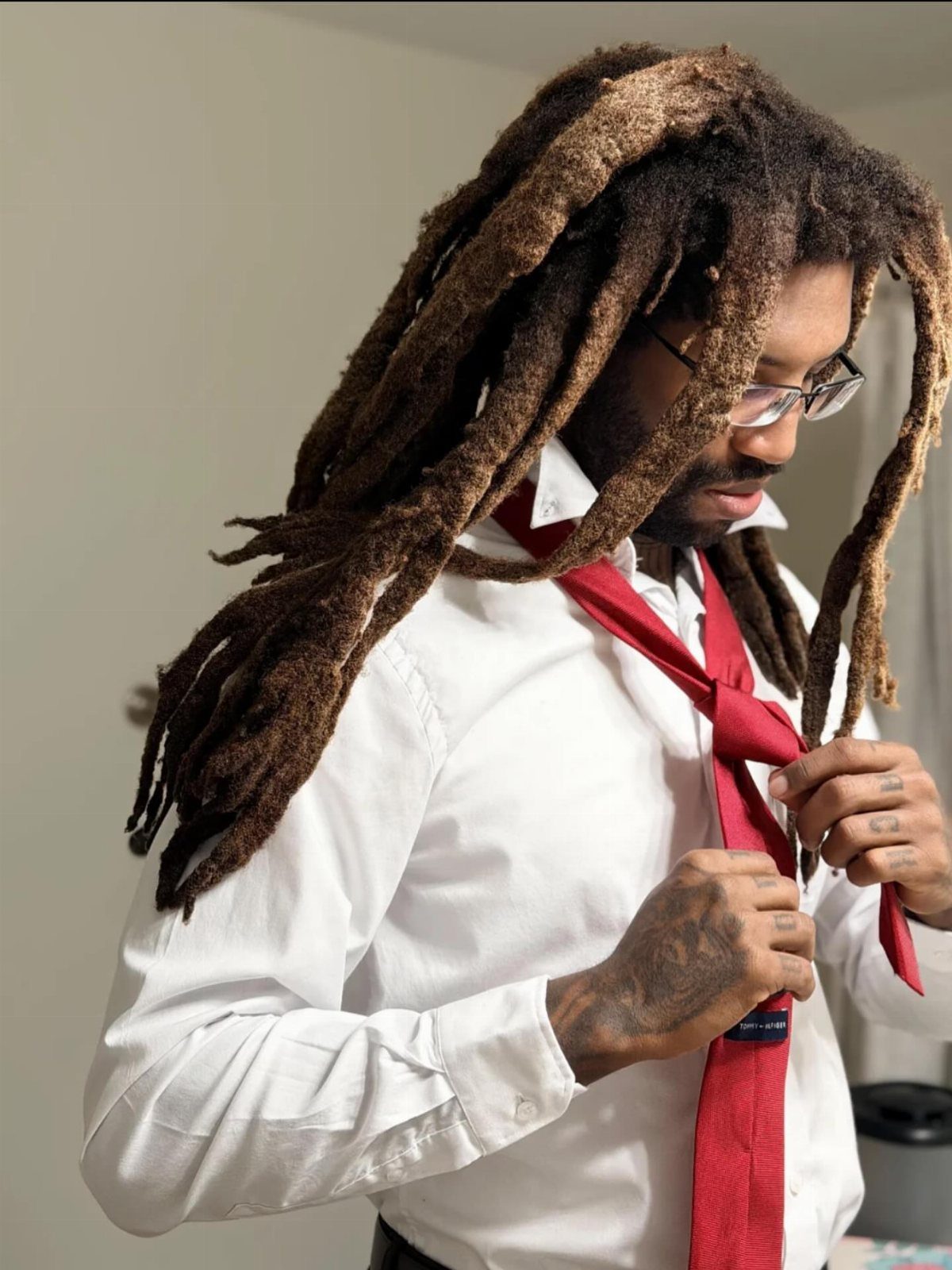 Man with long brown freeform dreadlocks wearing a white shirt and red tie.