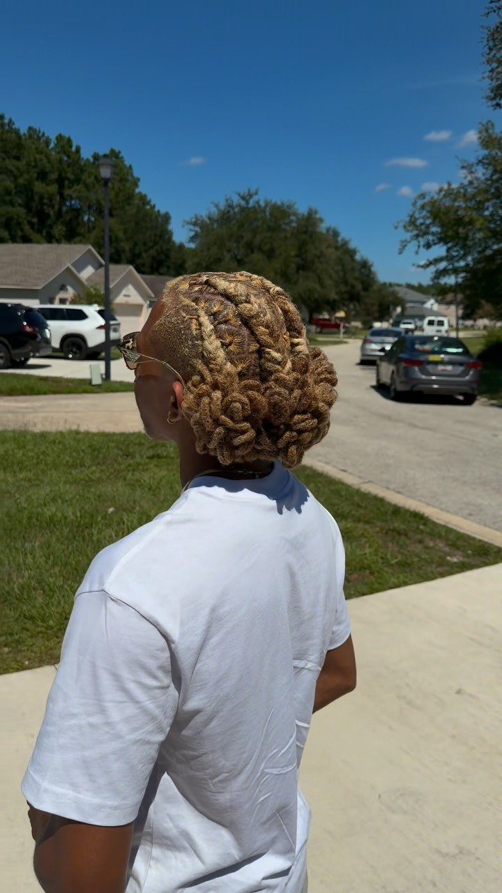Man with blonde long locs styled into a man bun wearing a white shirt.