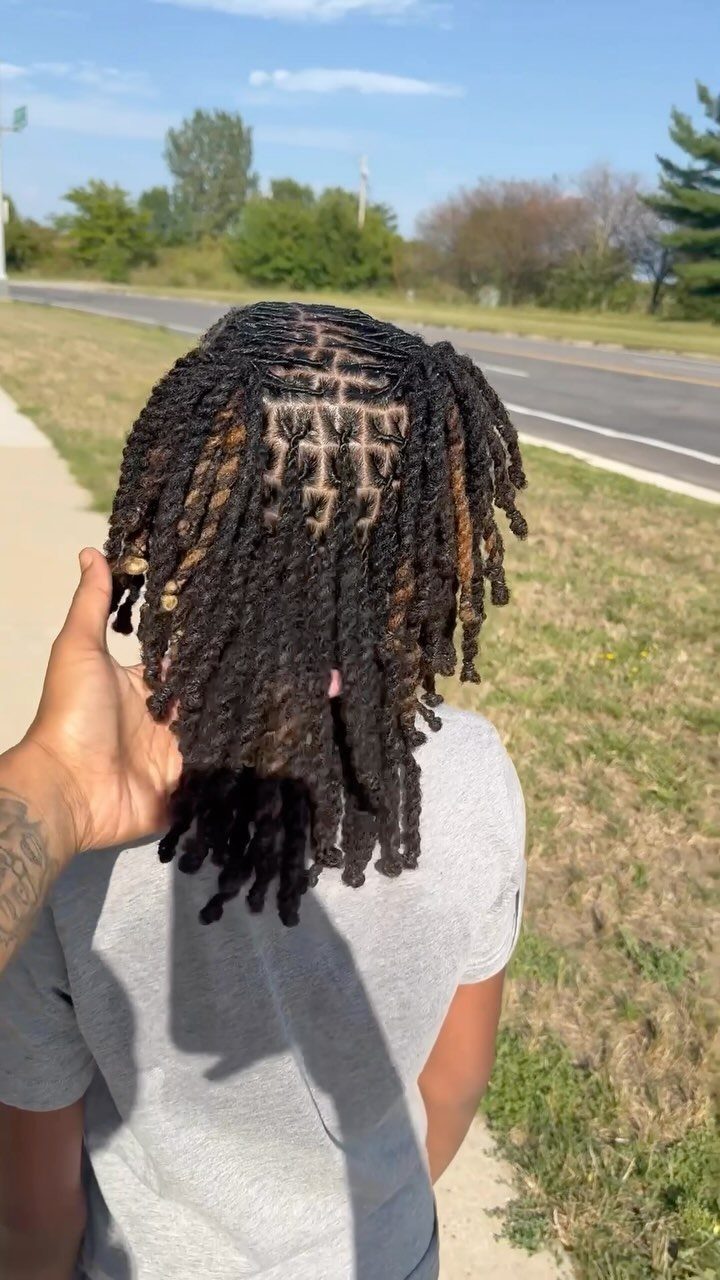 Man with medium length dark brown dreadlocks parted into neat rectangular sections.