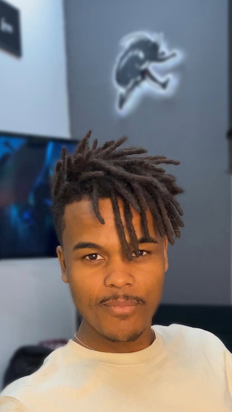Young man with short, upright dark brown dreadlocks leaning forward over his forehead.