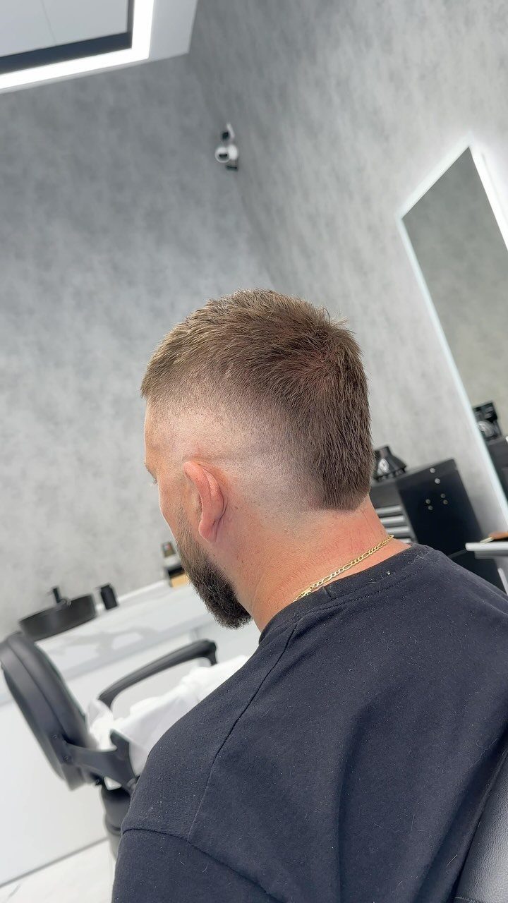 Man with a buzz cut fade and groomed beard in a barbershop.