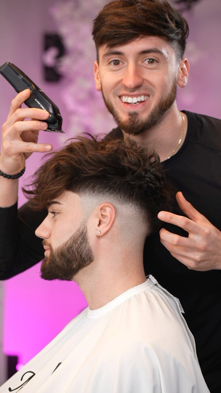 Man with a drop fade haircut and beard posing with his barber.